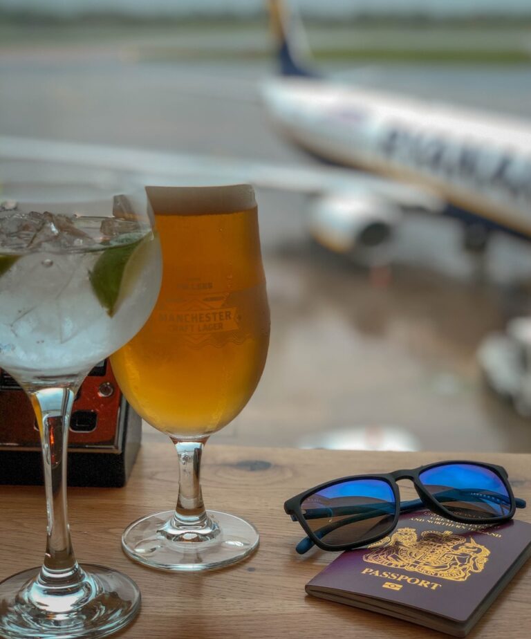 passport and beer in airport with airplane behind.