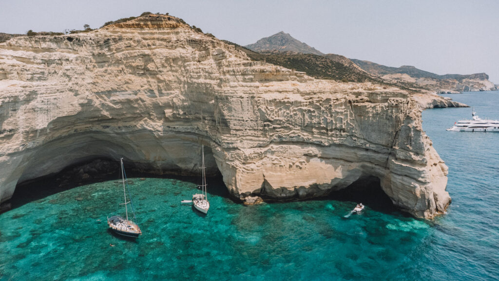 two sailboats floating in blue waters beneath white cliffs in Milos Greece 2 week itinerary