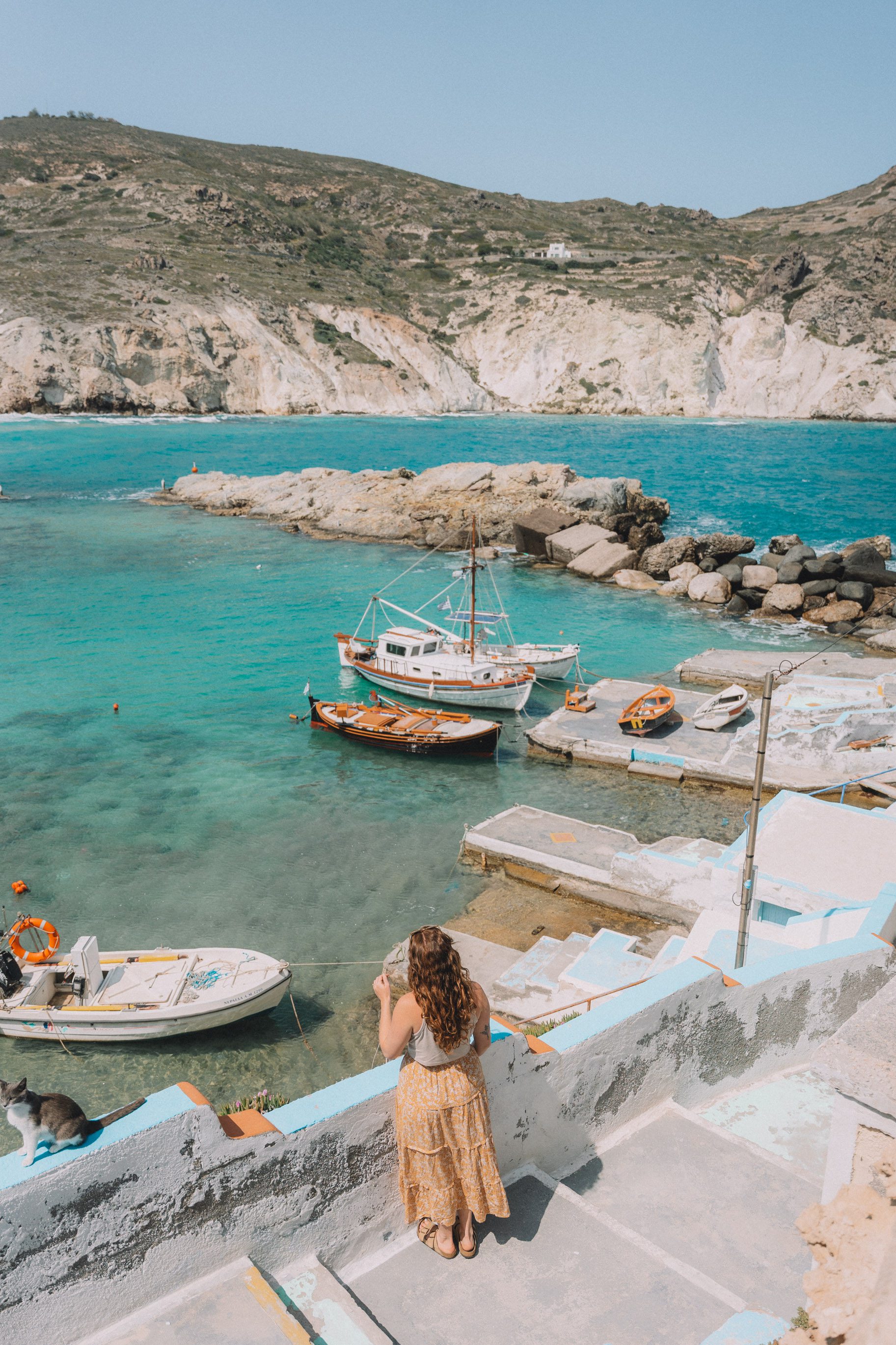 woman looking over boats anchored in blue water in Milos Greece 2 week itinerary