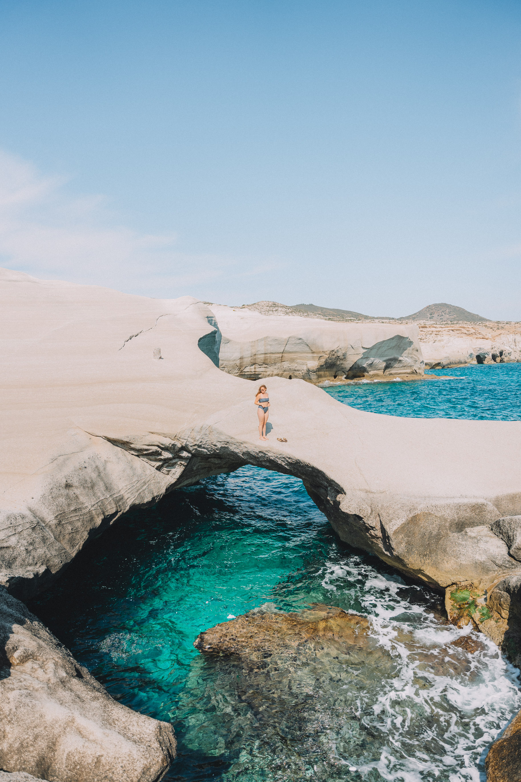 woman standing on natural bridge over blue water in Milos Greece 2 week itinerary