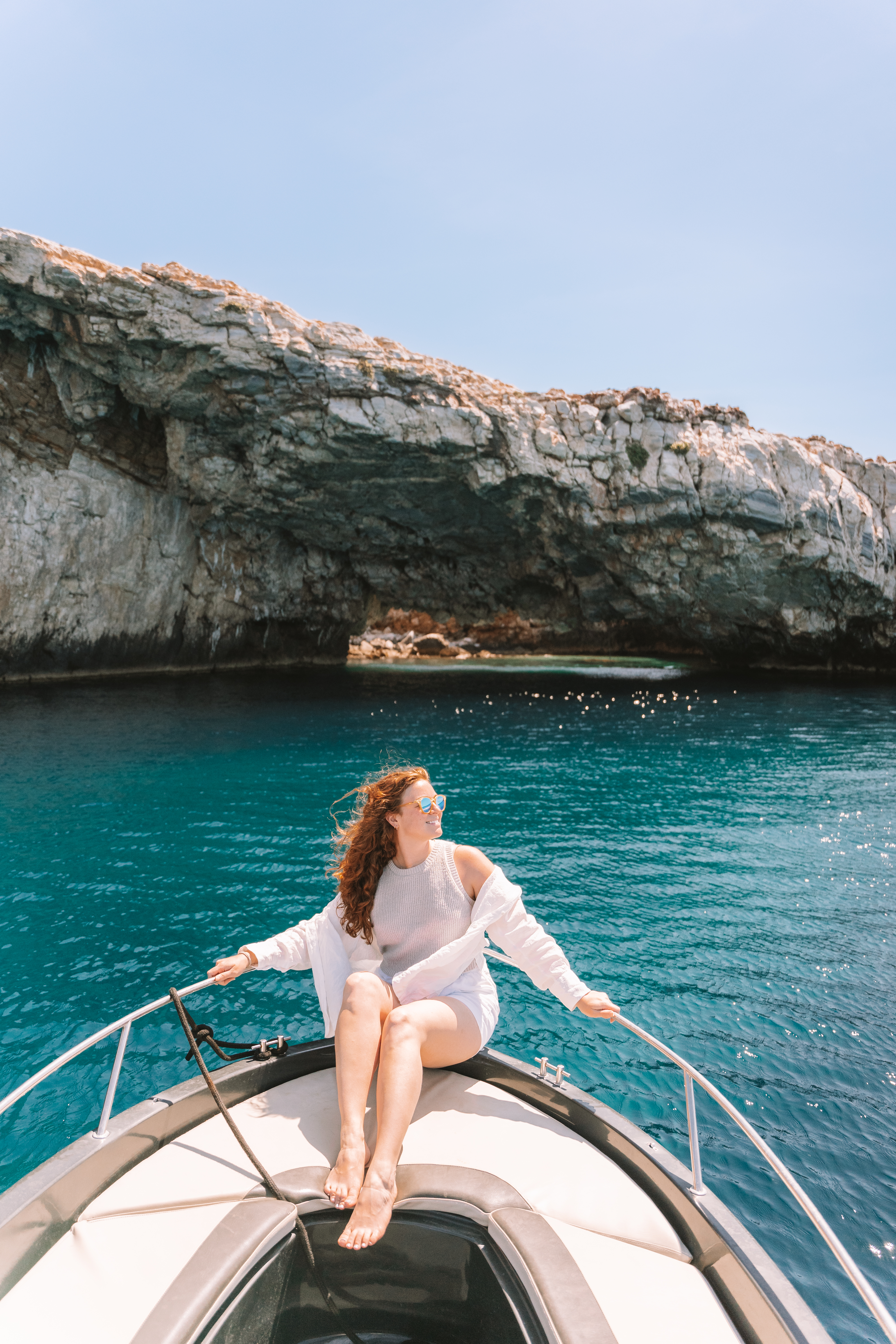 woman sitting at prow of boat in front of natural made rock bridge paros greece 2 week itinerary