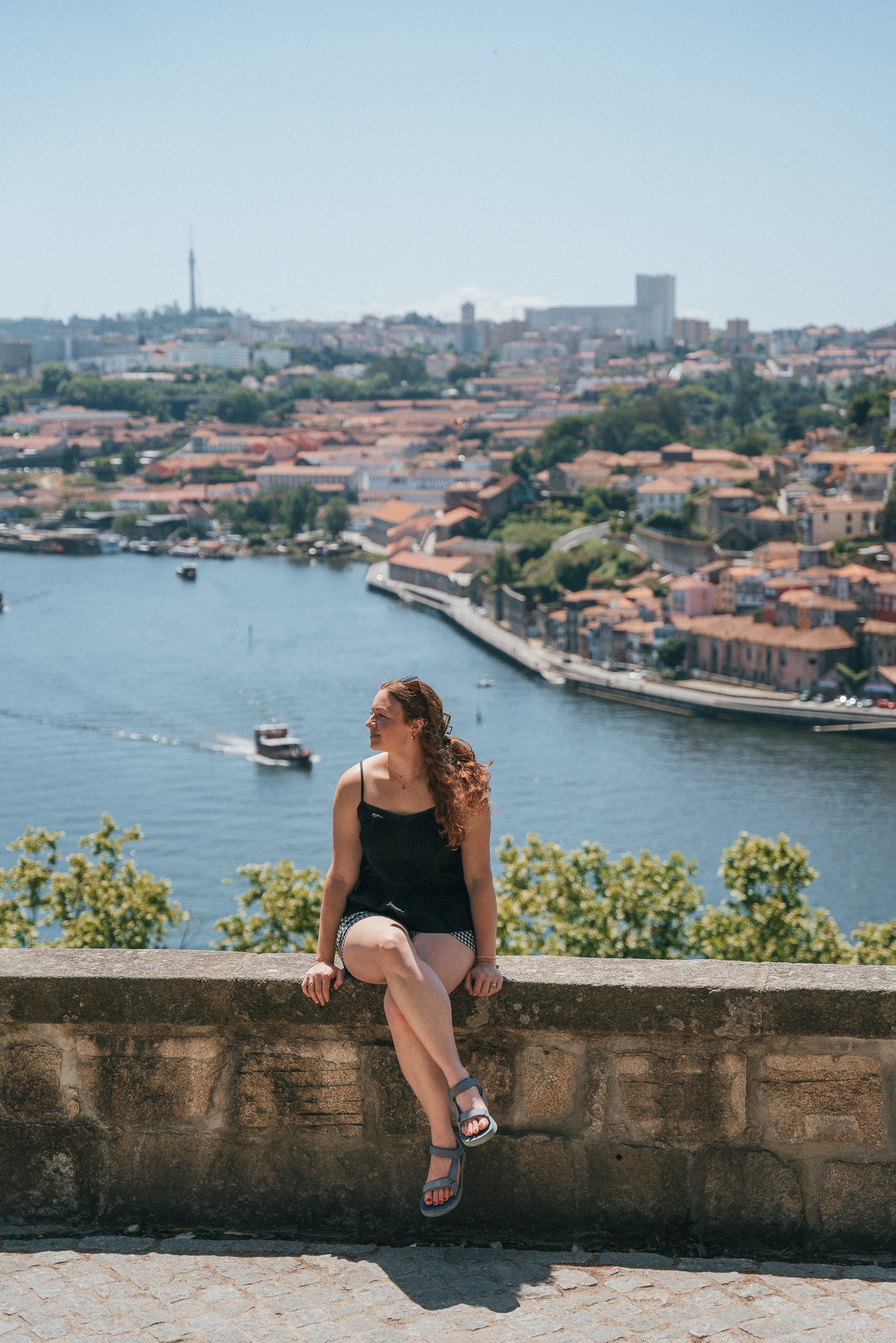 woman sitting on stone wall overlooking Porto skyline and Douro River from Jardim do Cristal in Porto Portugal 2 day Porto itinerary